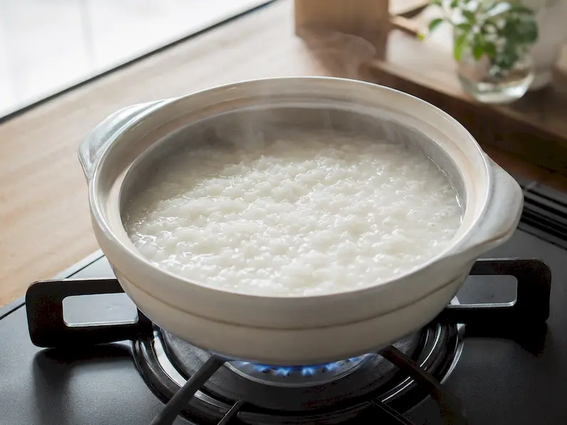 小鍋の中で塩麹のお粥が弱火でやさしく煮えているイメージ