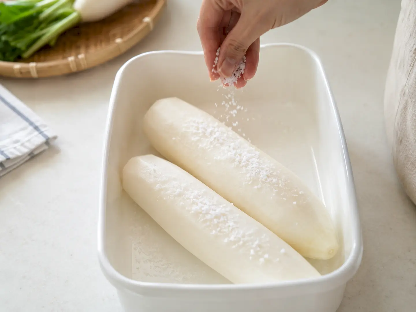 塩をすり込んだ大根2本を容器に並べ、残った食塩を上から振りかける工程