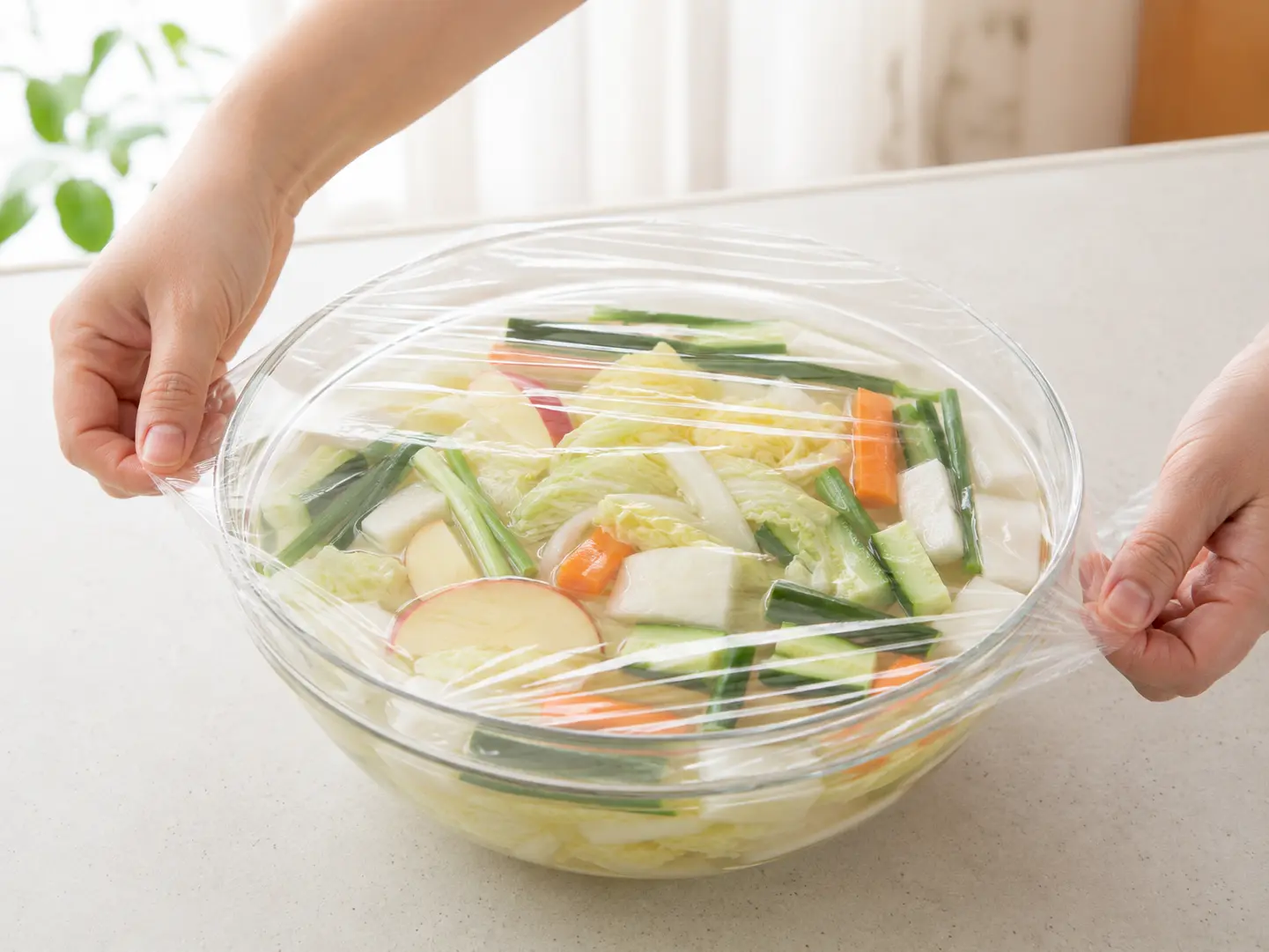 水キムチ液と野菜が入った透明ボウルへラップをかけている工程