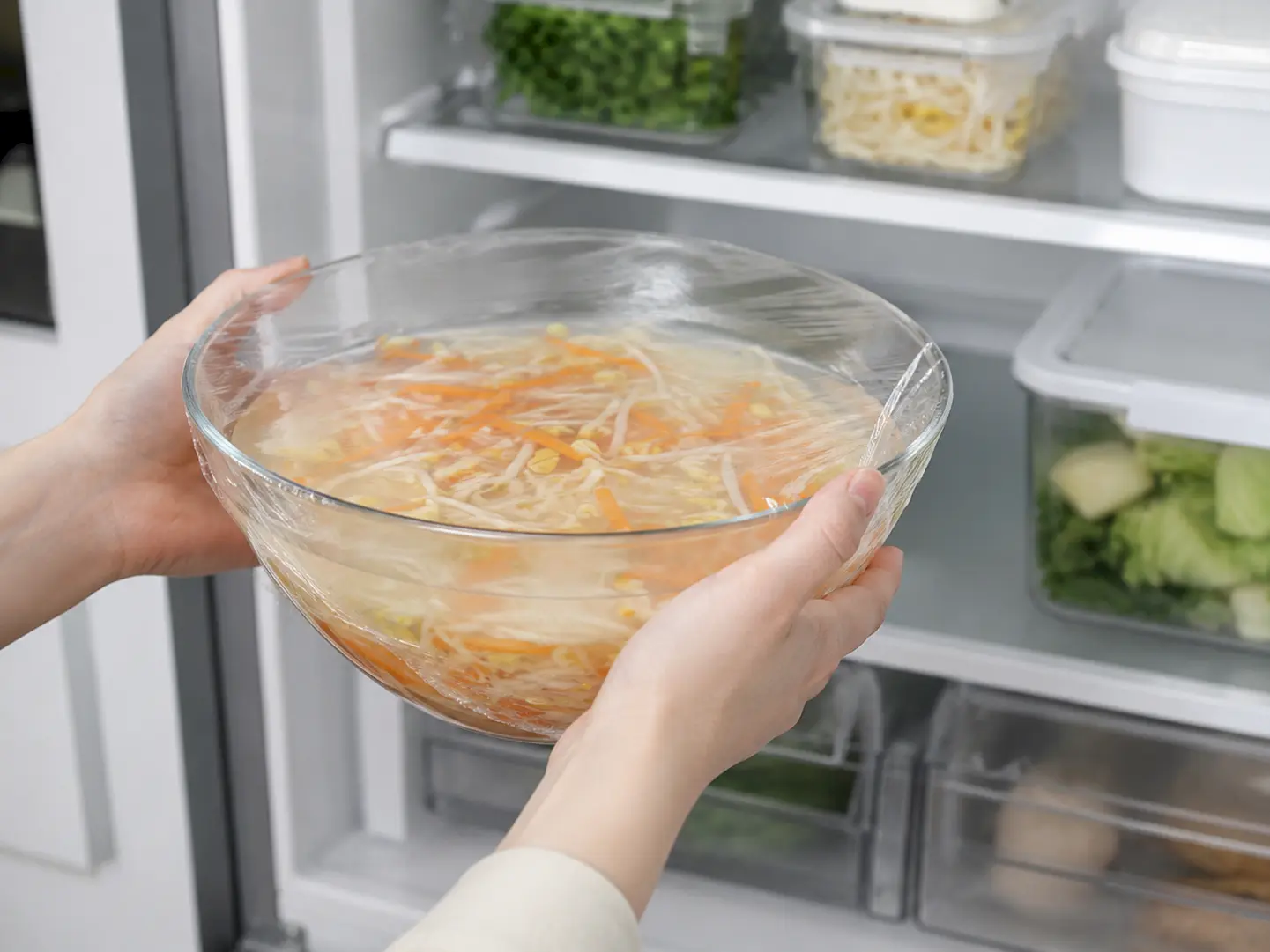 ラップをした冷製もやしの水キムチを家庭用冷蔵庫へ入れている工程