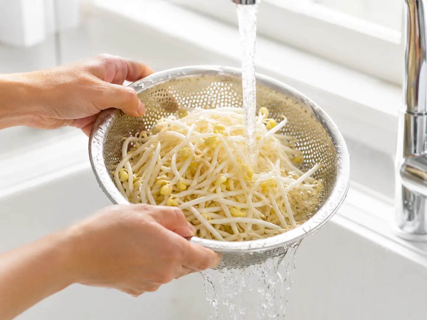 新鮮なもやしをざるに入れて流水でやさしく洗っている工程