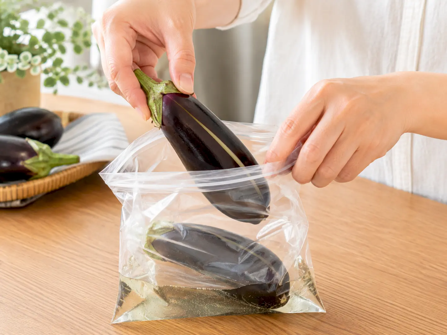 切れ目を入れたなす2本を漬け液の入った保存袋へ入れている工程