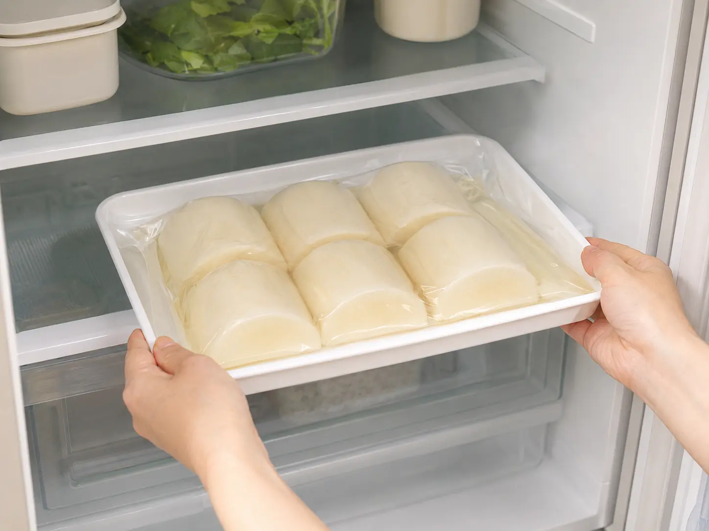 大根入りの食品用ポリ袋を載せた容器を冷蔵庫の棚へ水平に置く手元
