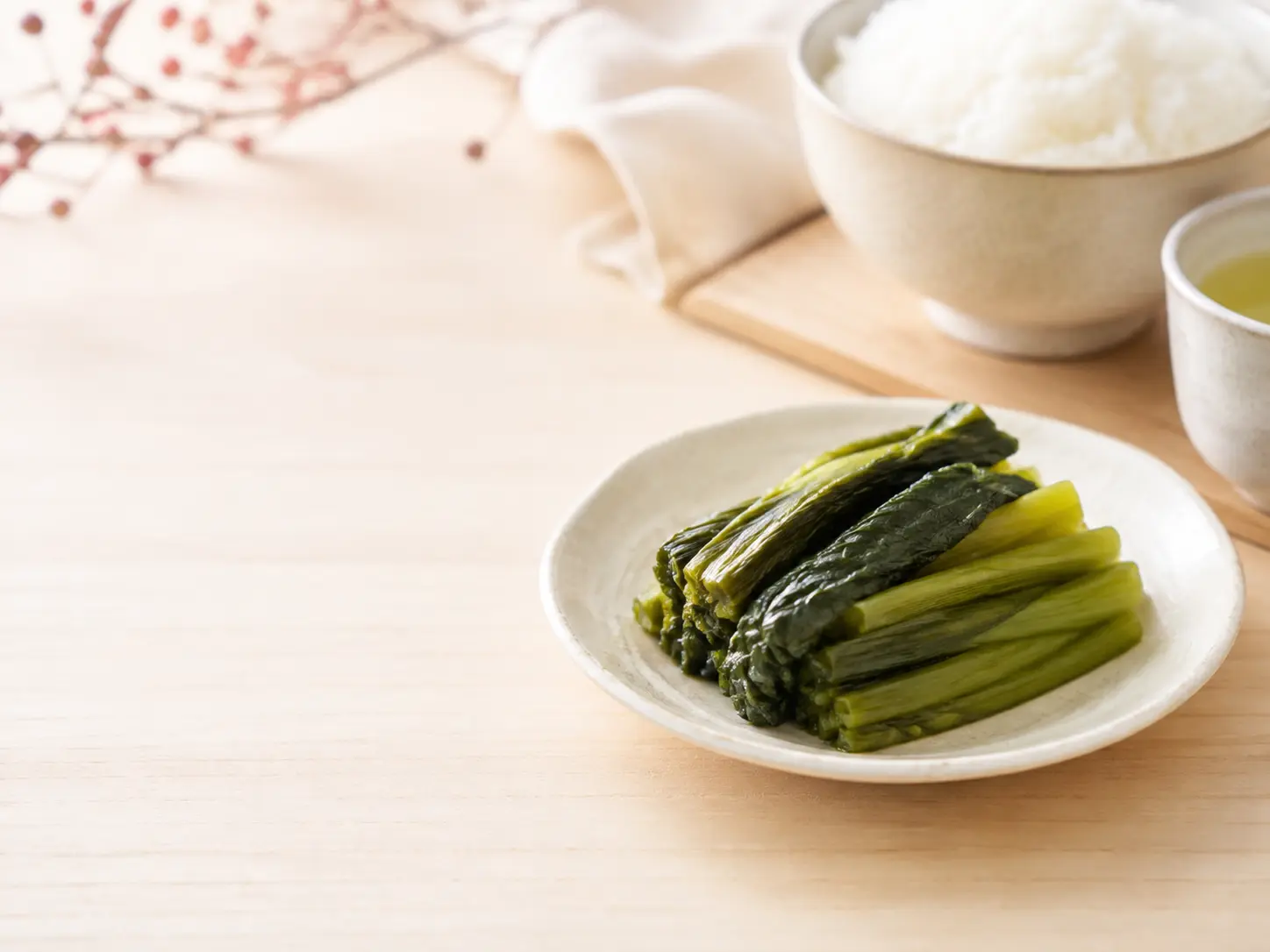 自然な緑色の野沢菜漬けを生成りの器へ盛り、ご飯と湯のみを添えた冬の食卓
