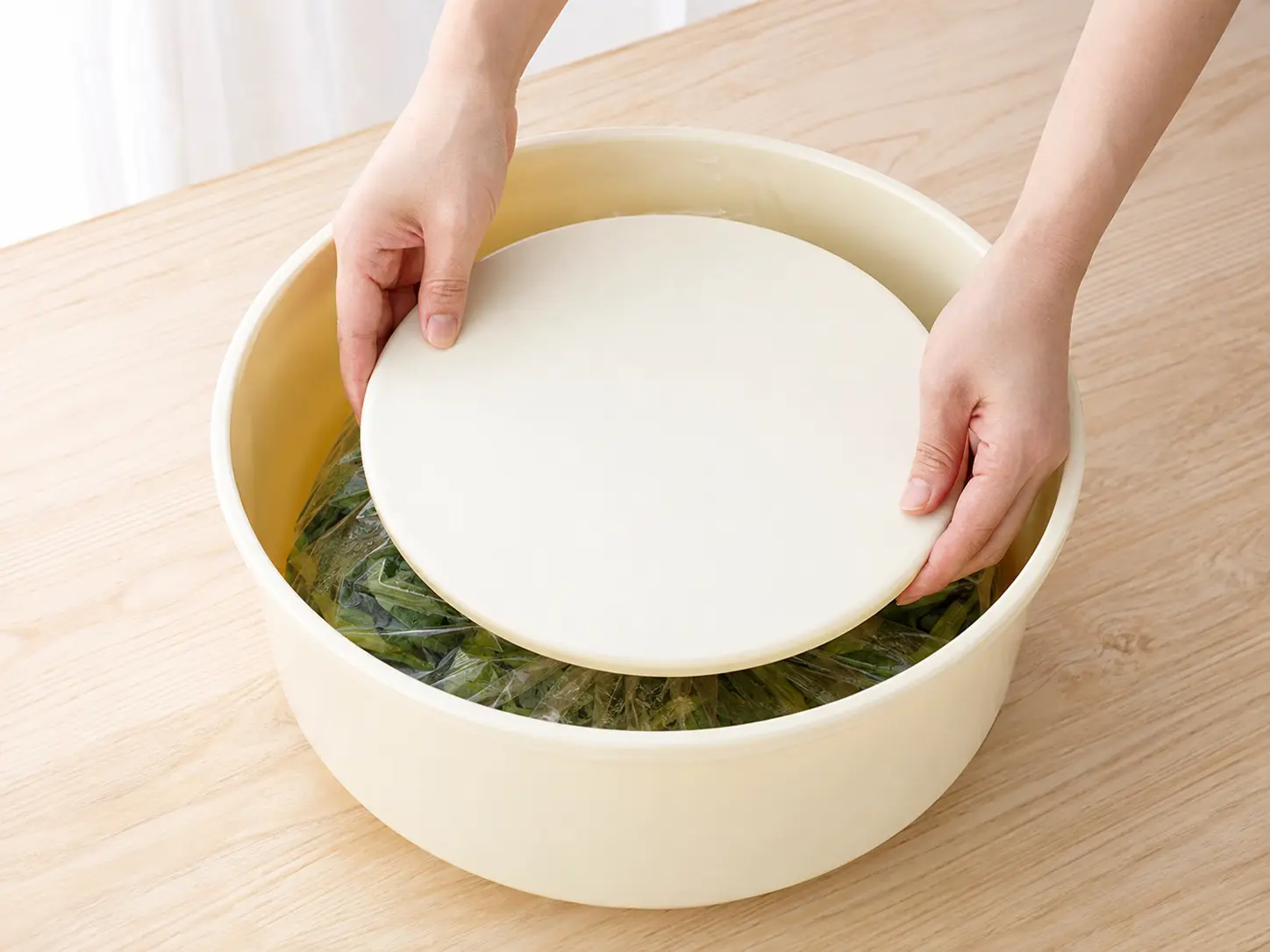 袋を閉じた野沢菜の上へ押しぶたを水平に置く手元