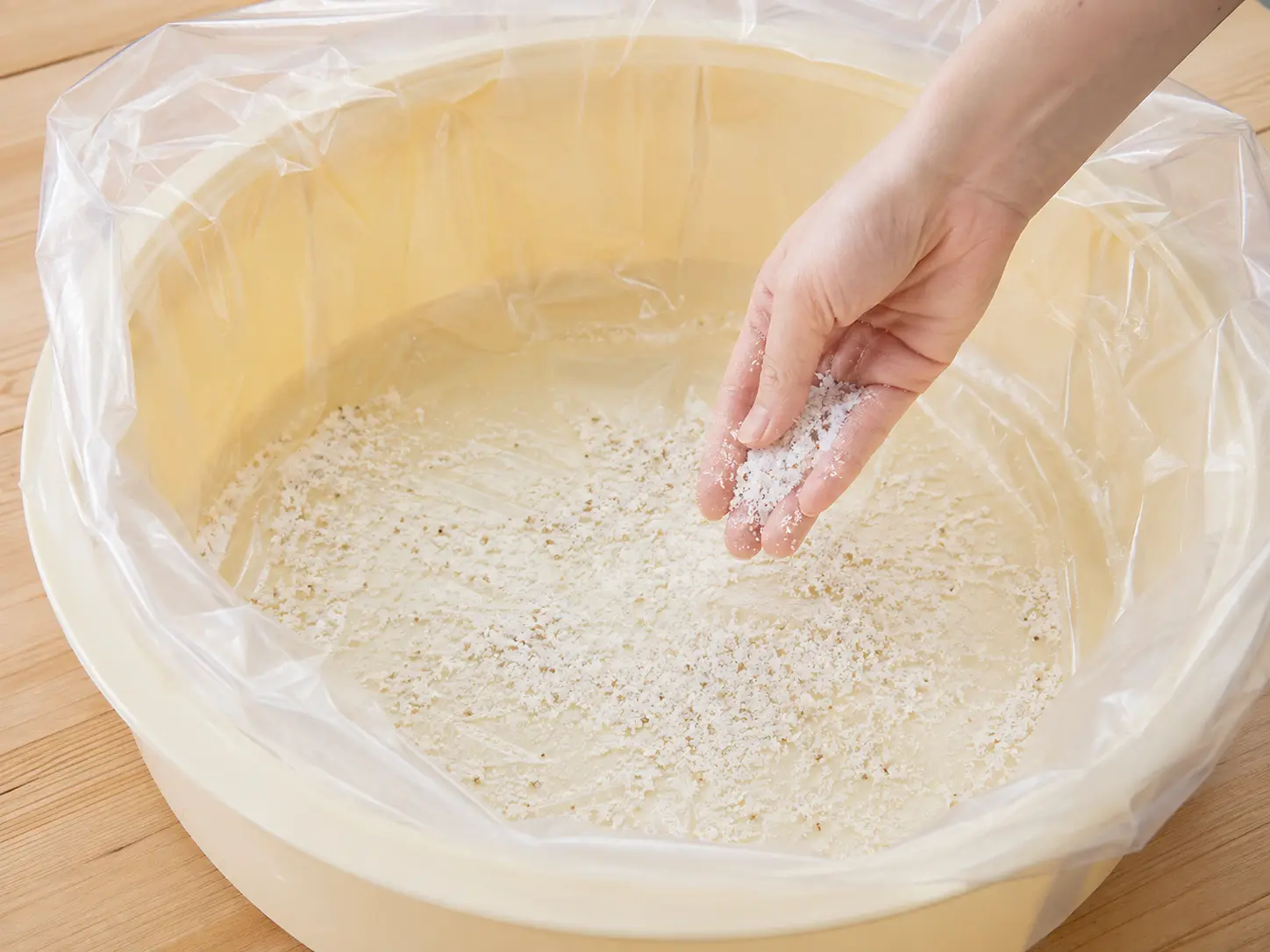 食品用ポリ袋を敷いた容器の底へ混合塩をひと握り振り入れる手元