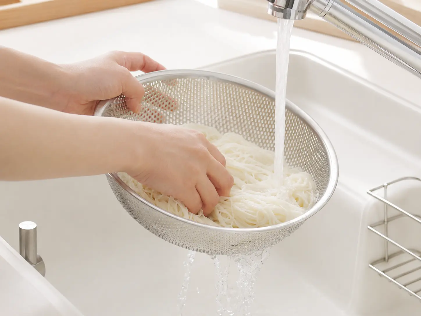 ゆでたそうめんをざるに取り、流水でよく冷やして水気を切っている手元