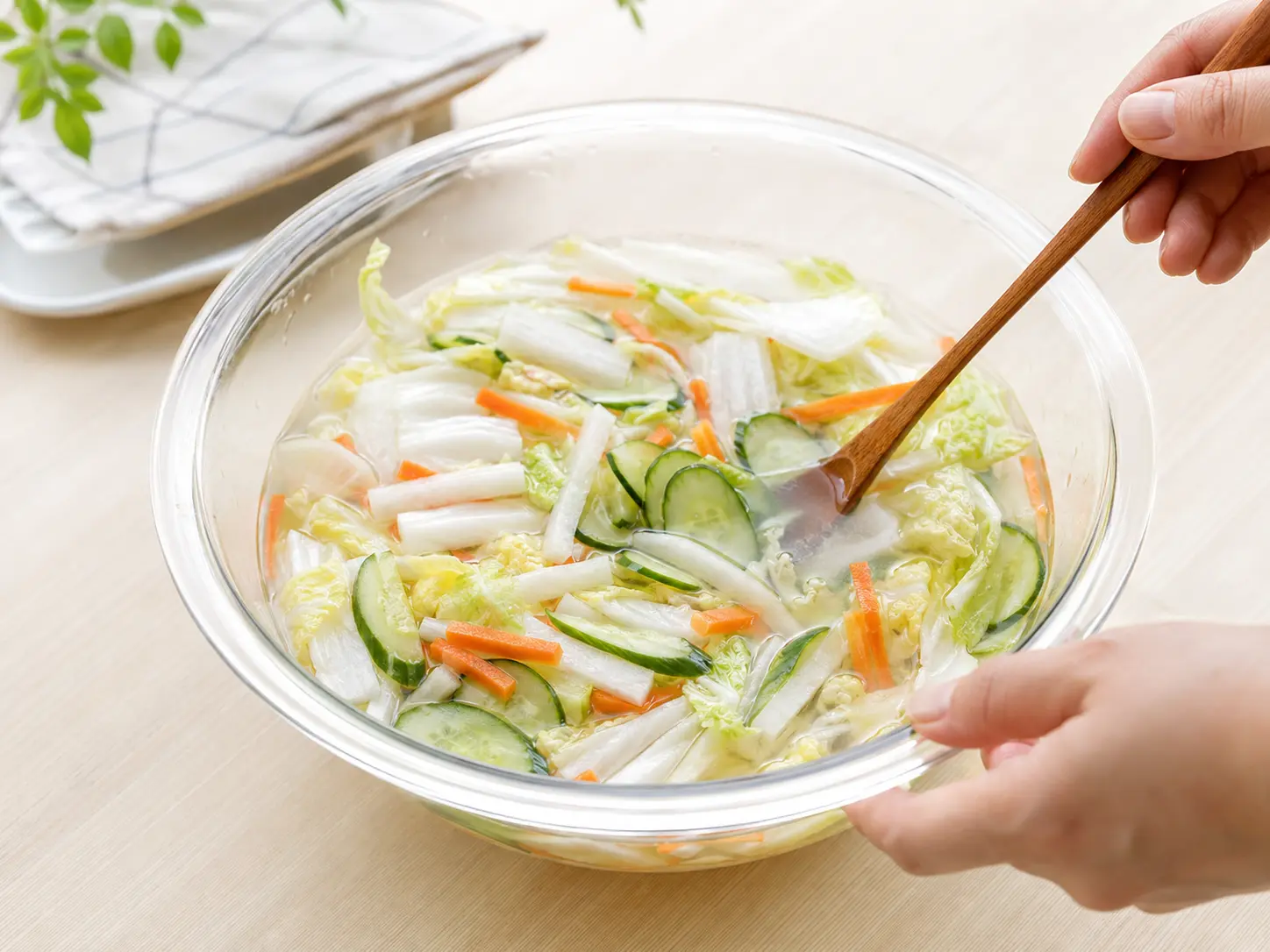 透明なボウルで水と冷んやり水キムチの素を混ぜ、切った野菜を加えている手元