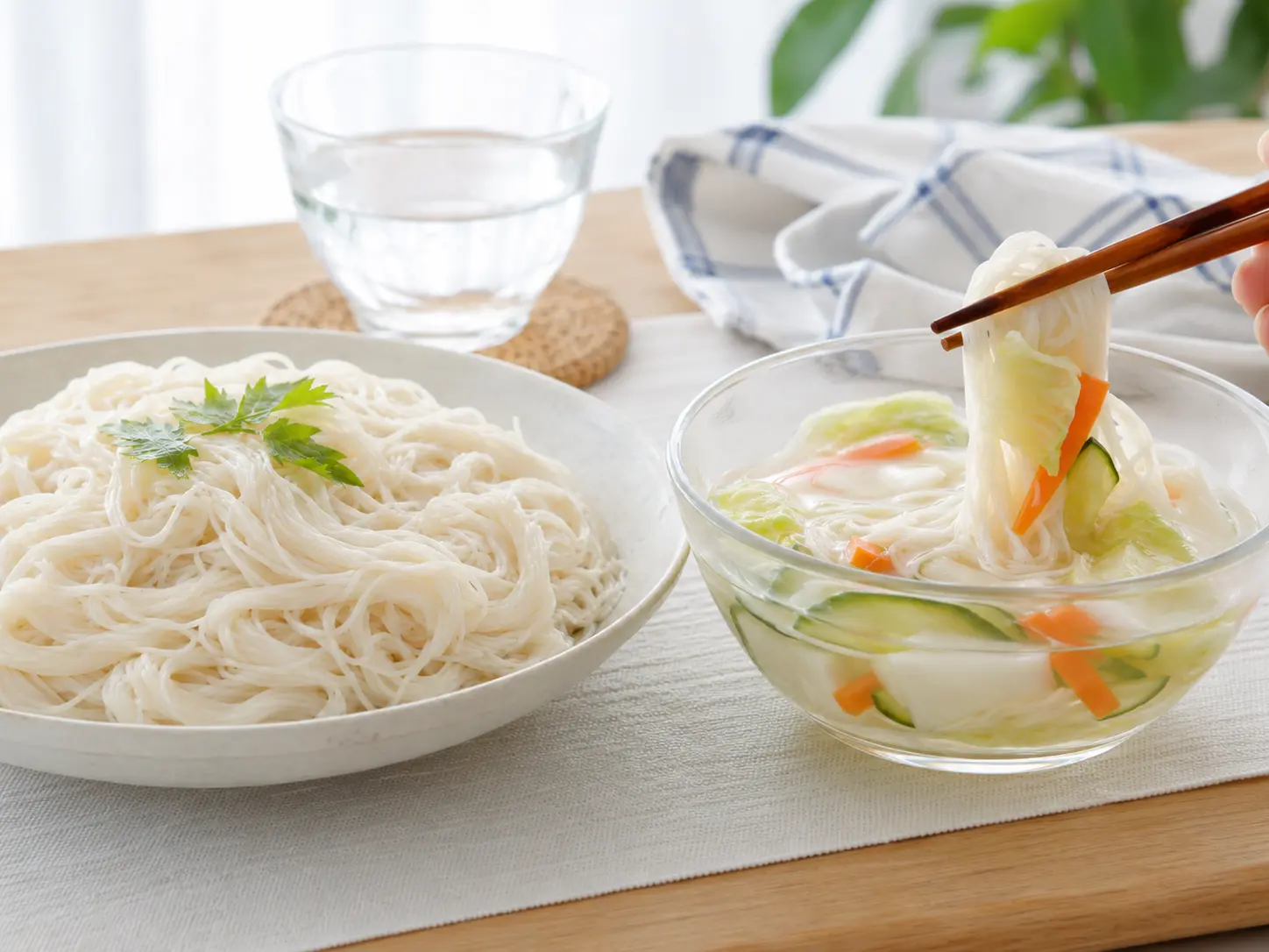 冷たいそうめんを箸で取り、澄んだ漬け汁と野菜が入った水キムチへつけている食卓