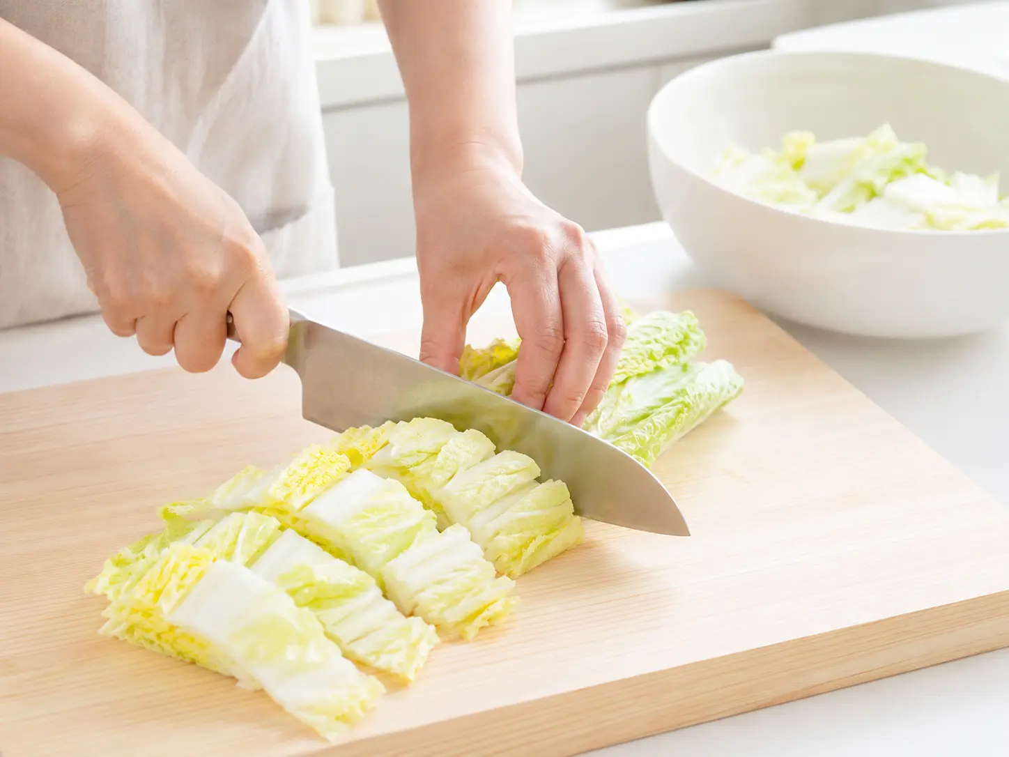 清潔なまな板の上で白菜を2から3センチ幅のざく切りにしている手元