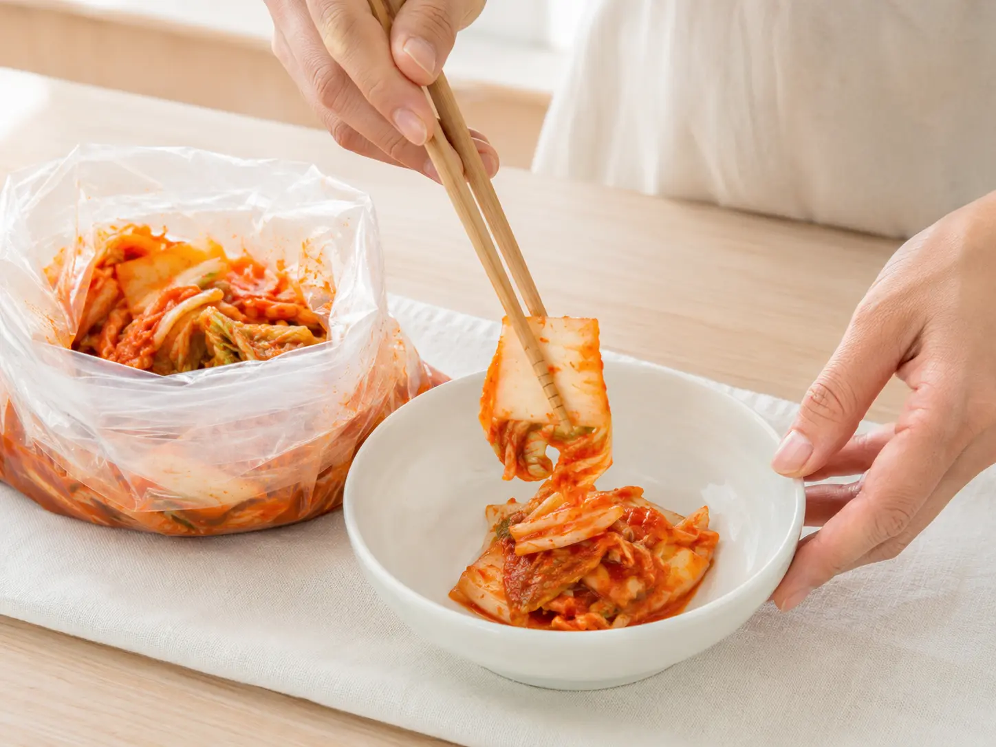 漬け上がった白菜キムチを清潔な箸で白い器へ盛り付けている手元