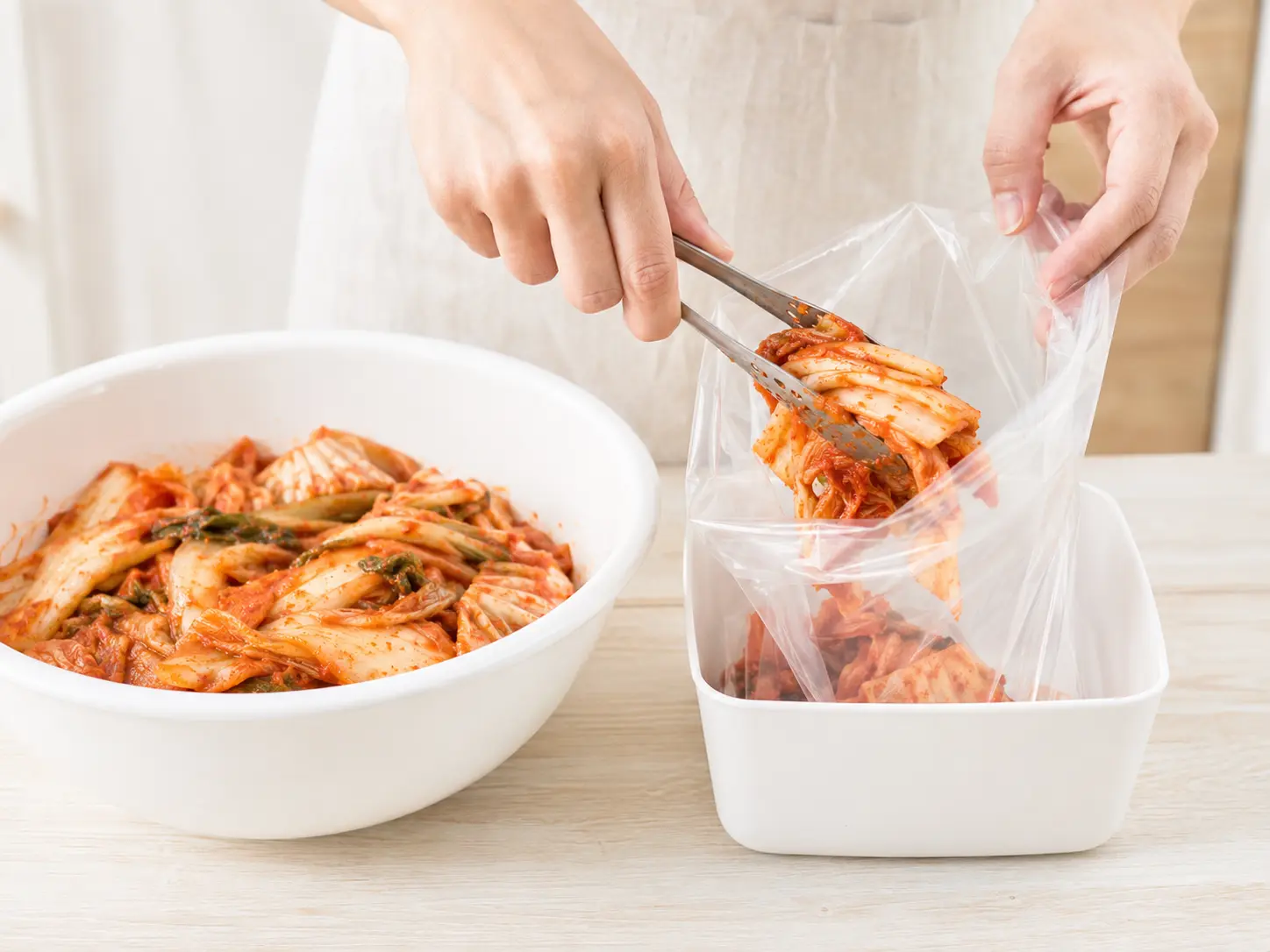 キムチ漬の素を混ぜた白菜を透明な食品用ポリ袋へ移している手元