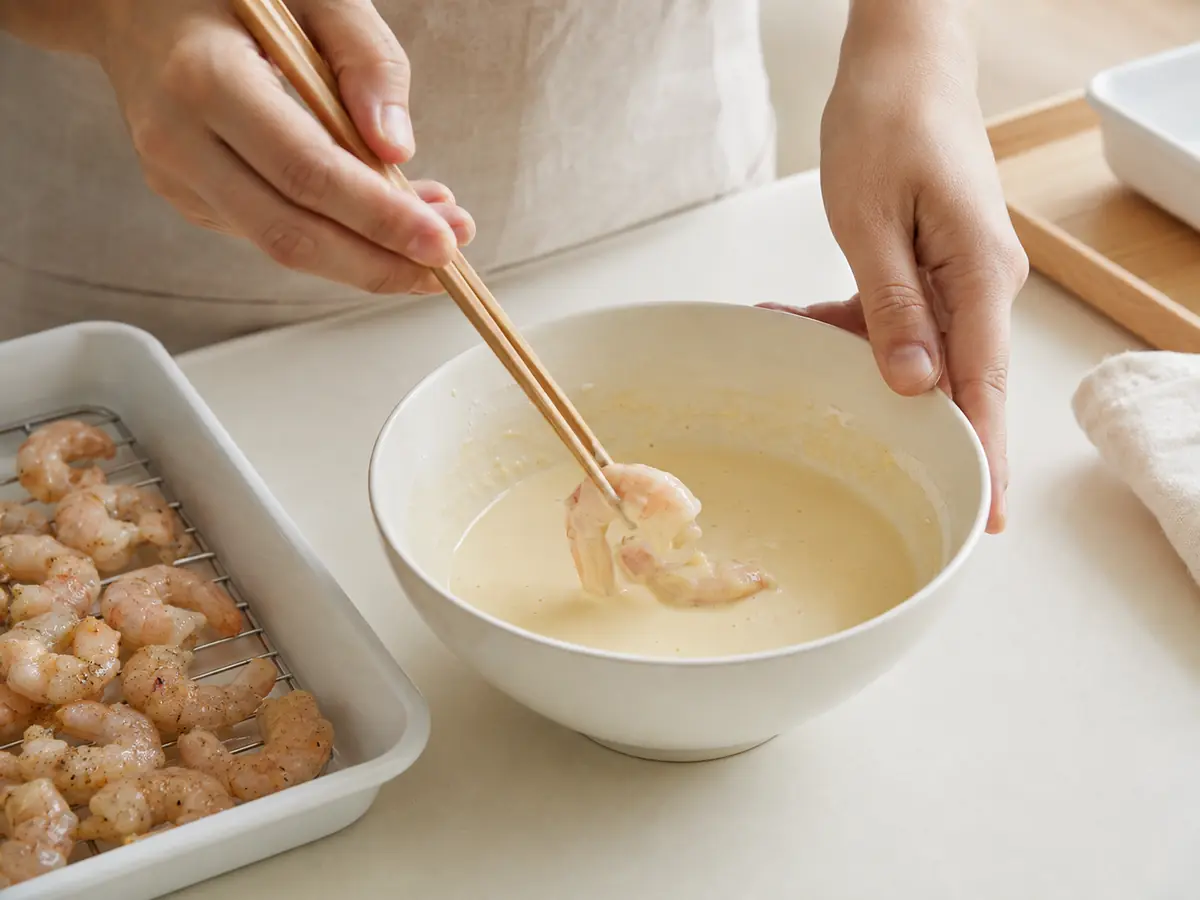 水気を拭いて下味を付けた小海老へ薄い天ぷら衣を付けている工程