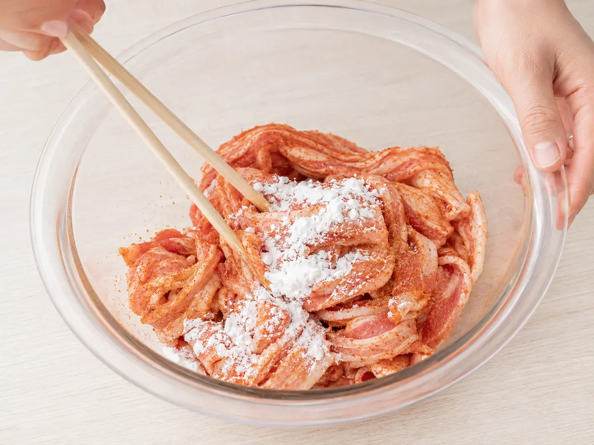 下味を付けた豚バラ薄切り肉へ片栗粉を薄く均一になじませている工程