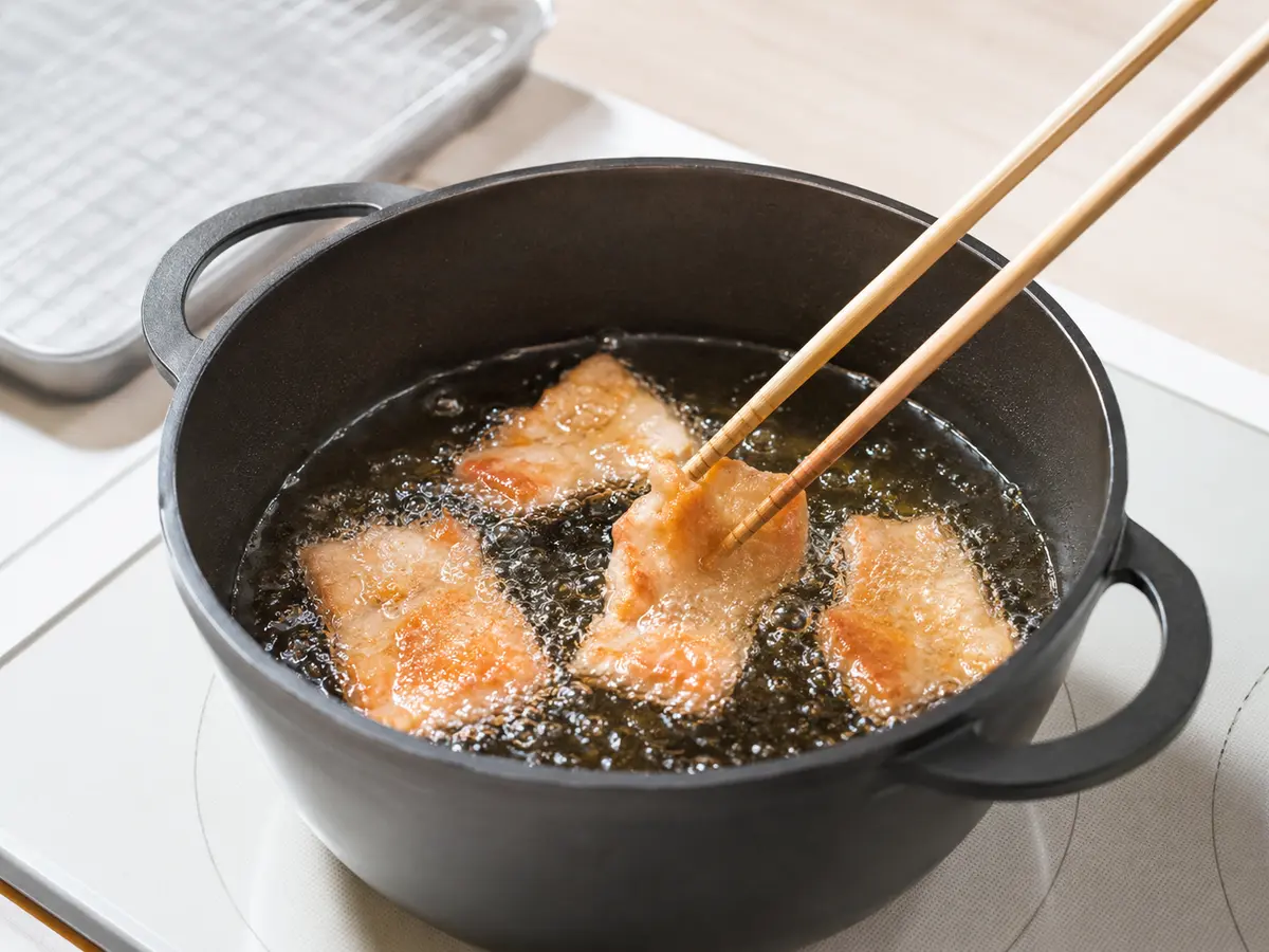 深さのある安定した鍋で豚バラ薄切り肉を180度の揚げ油へ適量ずつ入れている工程
