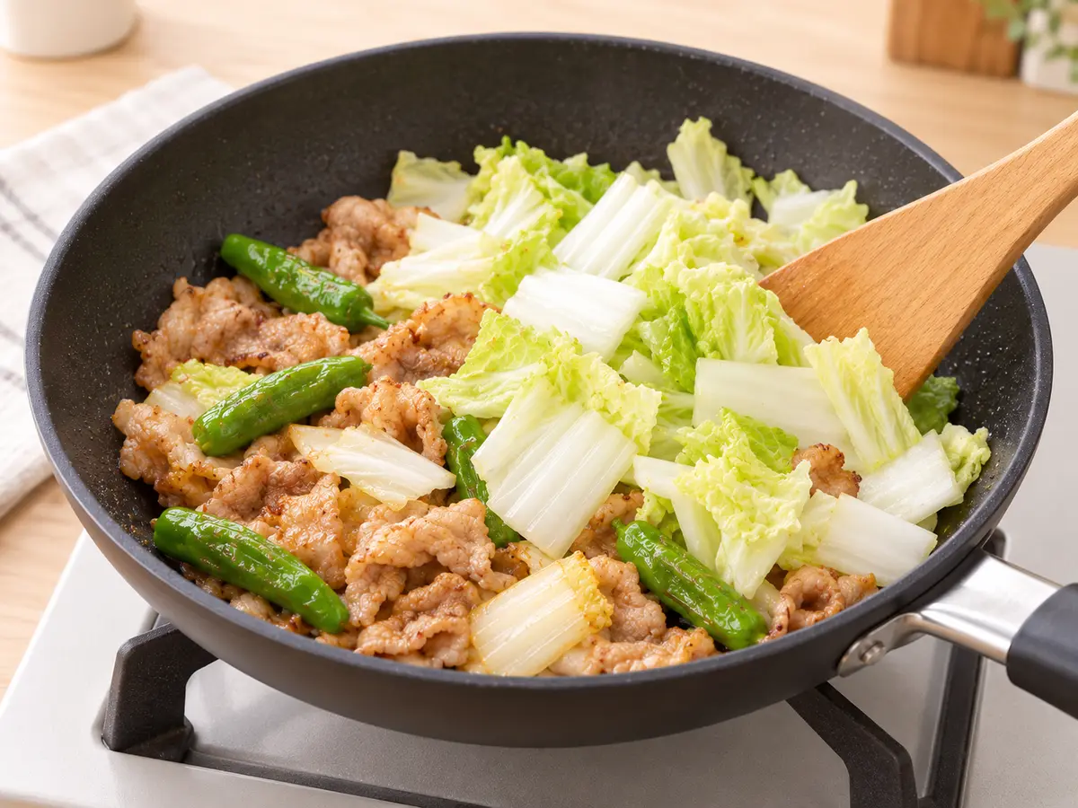 火の通った豚こま切れ肉としし唐辛子へ生の白菜を加える工程