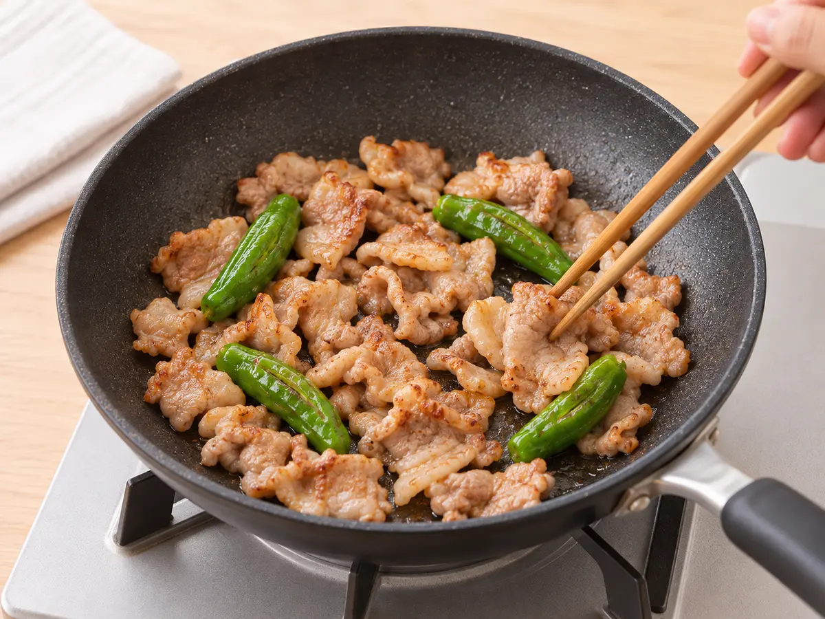 サラダ油を熱したフライパンで豚こま切れ肉としし唐辛子を炒める工程